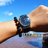 Person wearing a black wristwatch with a scenic background