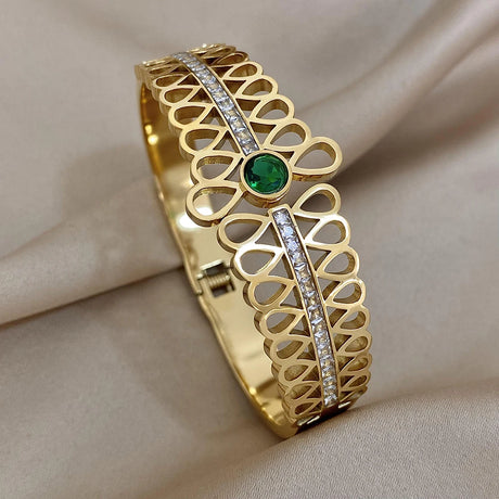 Gold bracelet with green gemstone and diamond accents on a beige fabric background