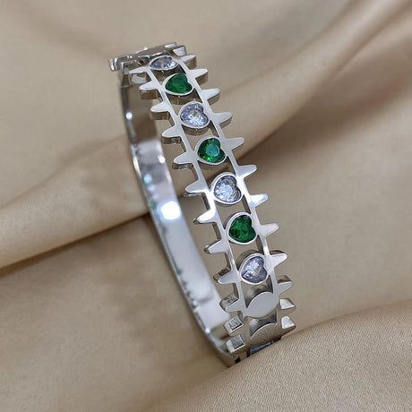 Silver bracelet with green and clear gemstones on a beige fabric background