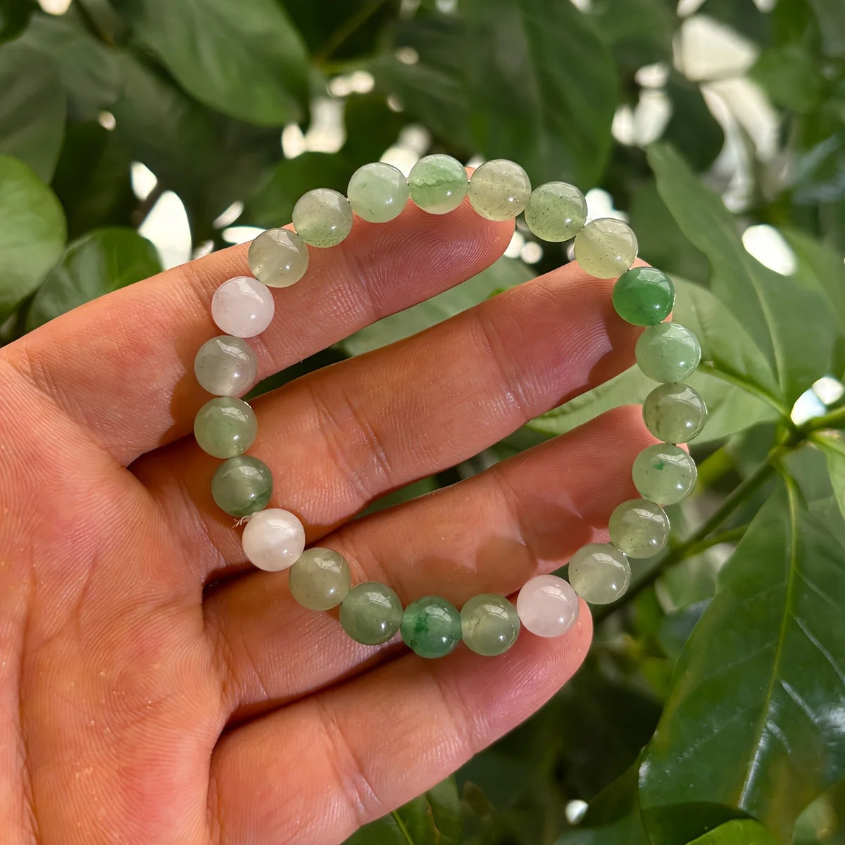Hand holding a green and white beaded bracelet with a natural background