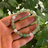 Hand holding a green and white beaded bracelet with a natural background
