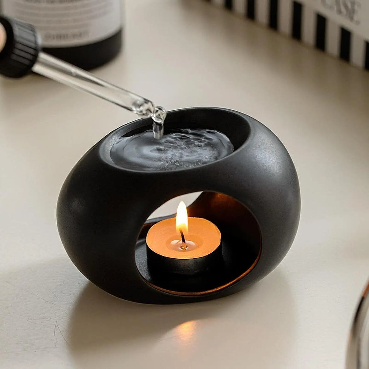 Black ceramic holder with a lit candle inside on a light surface