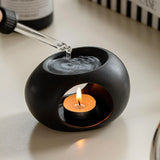 Black ceramic holder with a lit candle inside on a light surface