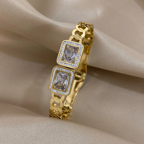 Gold bracelet with square gemstones on a beige fabric background