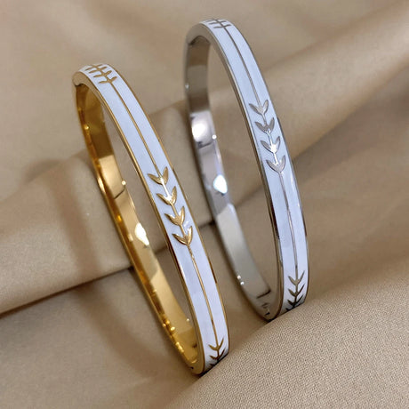 Two gold and silver bangles with leaf patterns on a beige fabric background