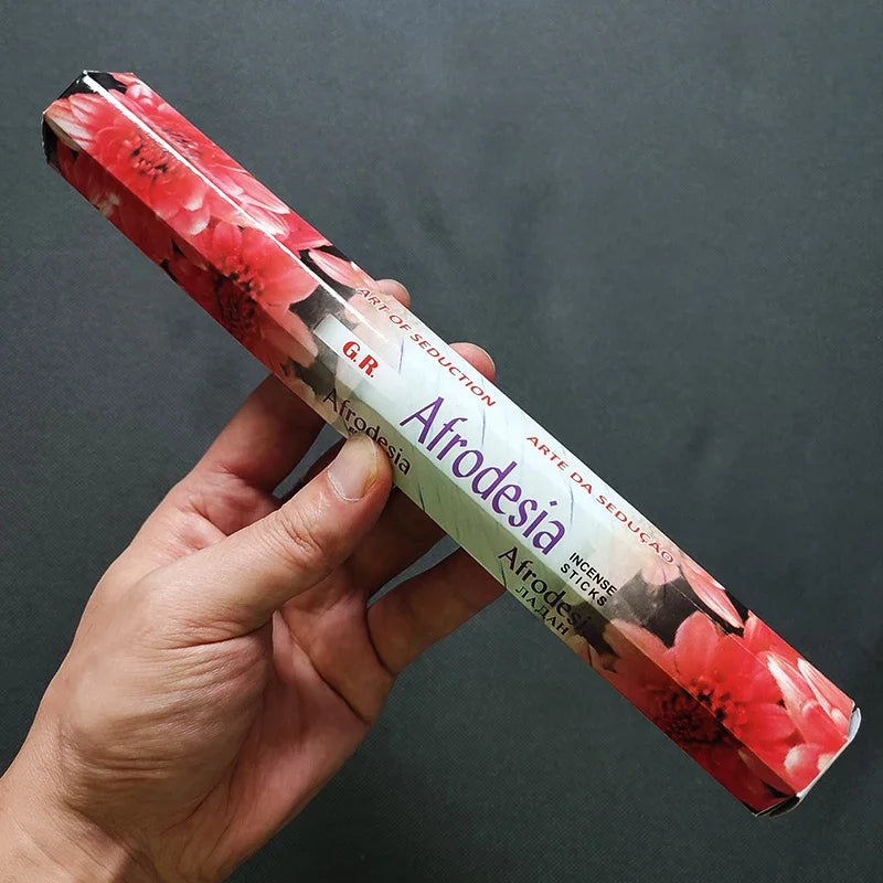 Hand holding a cylindrical product with 'Afrodesia' branding against a dark background
