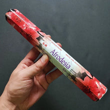 Hand holding a cylindrical product with 'Afrodesia' branding against a dark background