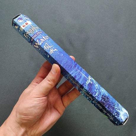 Blue incense box with text held by a hand against a dark background
