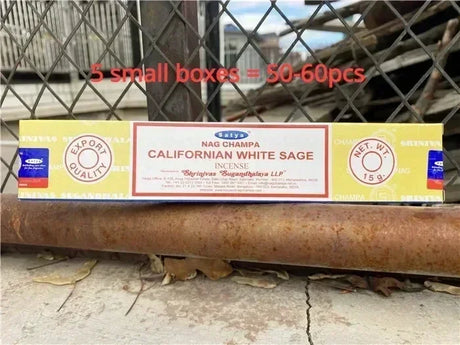 Box of Nag Champa Californian White Sage incense on a rusty metal surface with chain-link fence in the background.