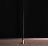 Brass incense stick holder with a single incense stick on a dark background