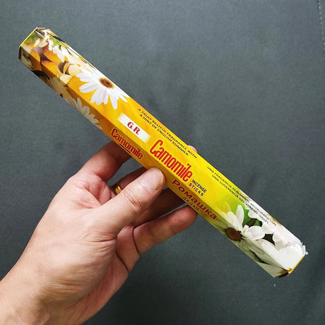 Hand holding a box of G.R. Camomile incense against a dark background