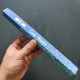 Hand holding a blue rectangular product labeled 'Cool Water' against a dark background