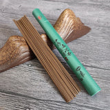 Green incense stick holder with incense sticks on a wooden surface