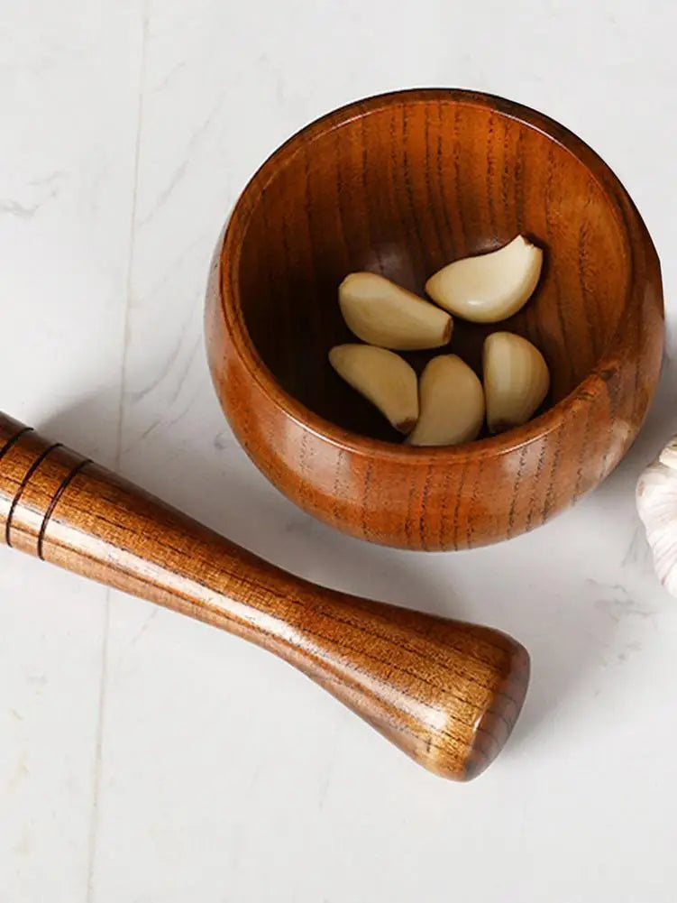 Wooden bowl with garlic cloves and a wooden pestle on a light background