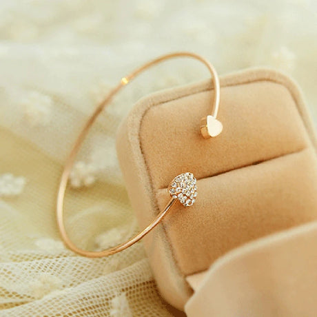 Gold bracelet with a heart-shaped charm on a beige fabric background