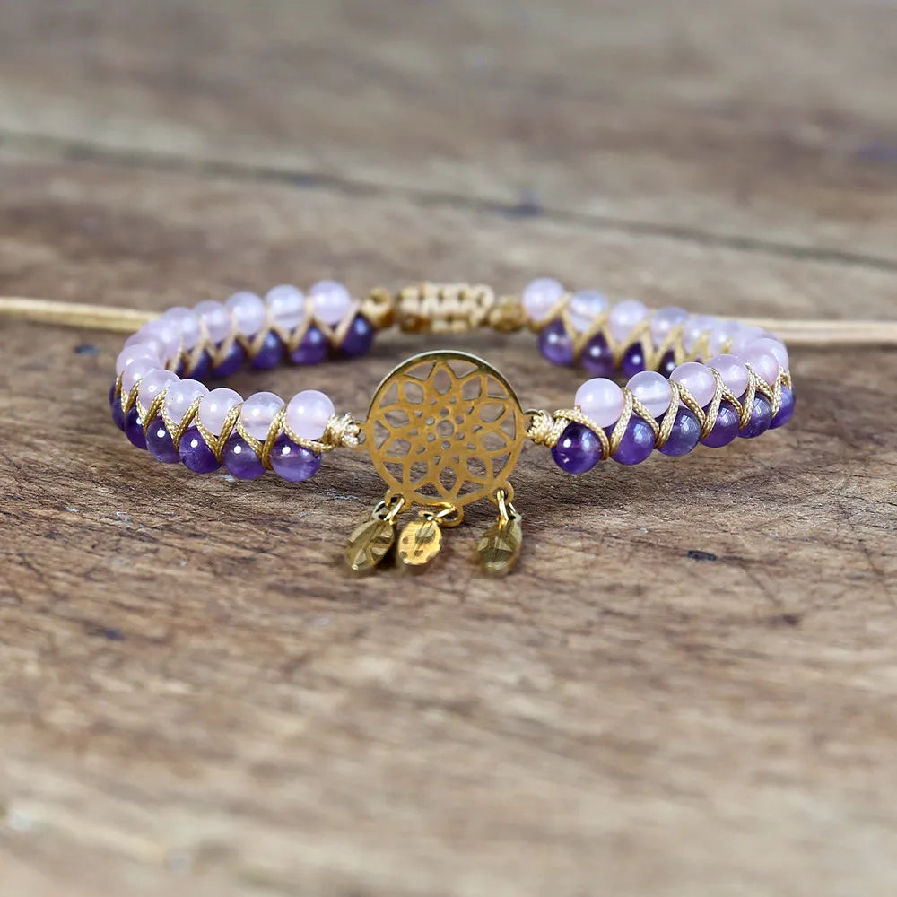 Bracelet with purple and white beads and a gold dreamcatcher charm on a wooden surface