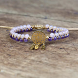 Bracelet with purple and white beads and a gold dreamcatcher charm on a wooden surface