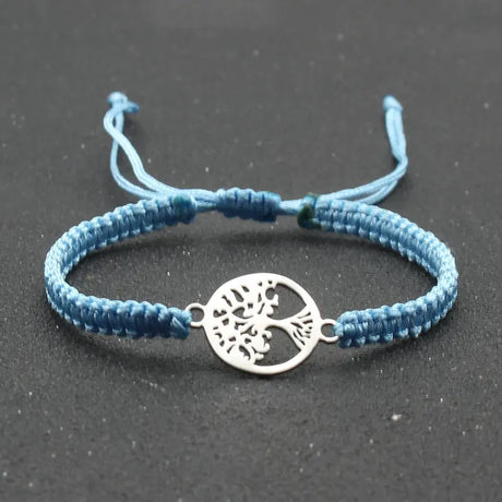 Blue braided bracelet with a silver tree of life charm on a dark background