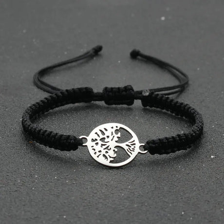 Black braided bracelet with a silver tree of life charm on a dark background