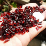 Hand holding red gemstones with a blurred natural background