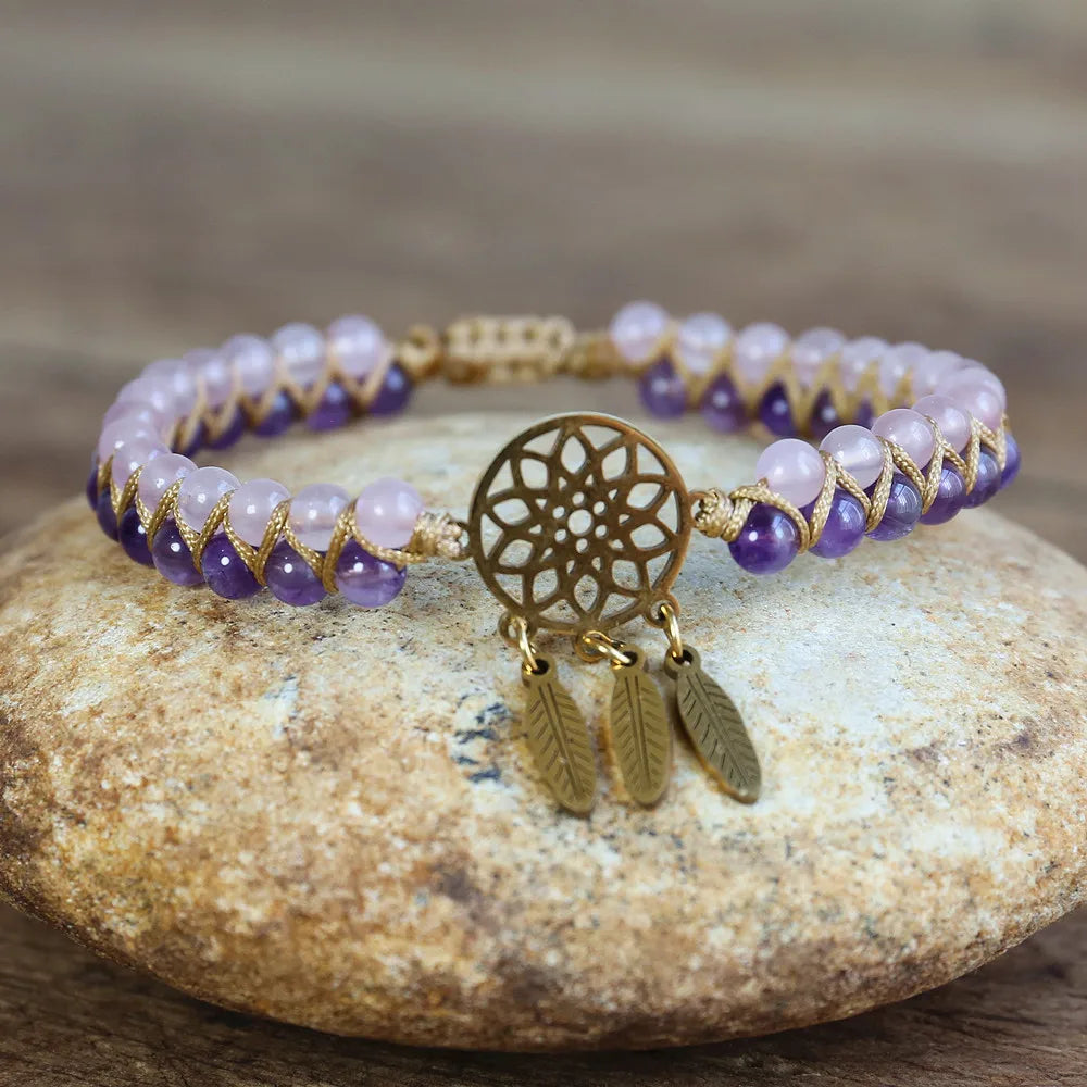 Bracelet with purple and white beads and gold dreamcatcher charm on a stone surface