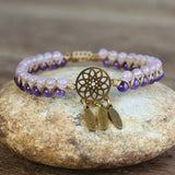 Bracelet with purple and white beads and gold dreamcatcher charm on a stone surface