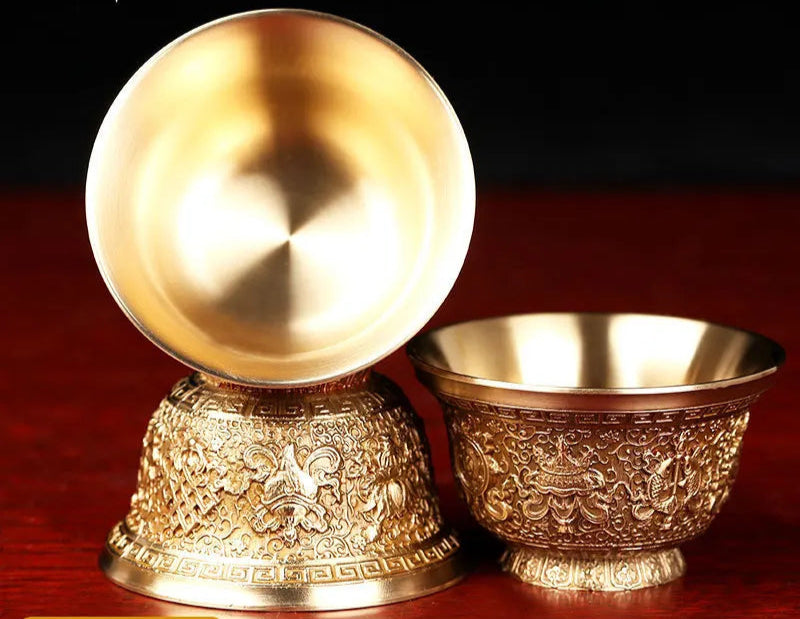 Two gold-colored bowls with intricate designs on a dark background