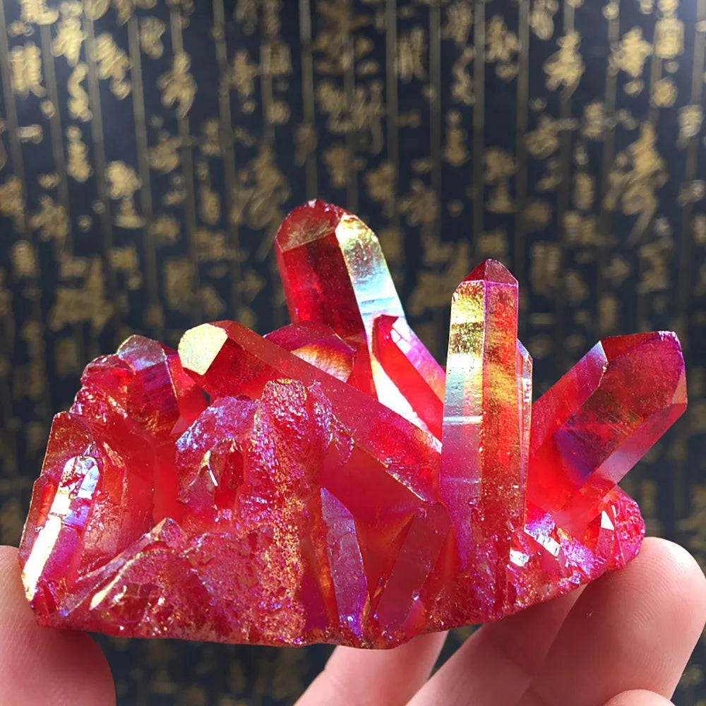Red and clear crystal formation held in a hand against a dark background with gold patterns.