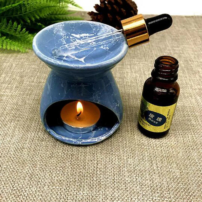 Blue ceramic oil burner with a lit candle and a bottle of essential oil on a textured surface.