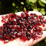Hand holding red garnet stones with a blurred green background