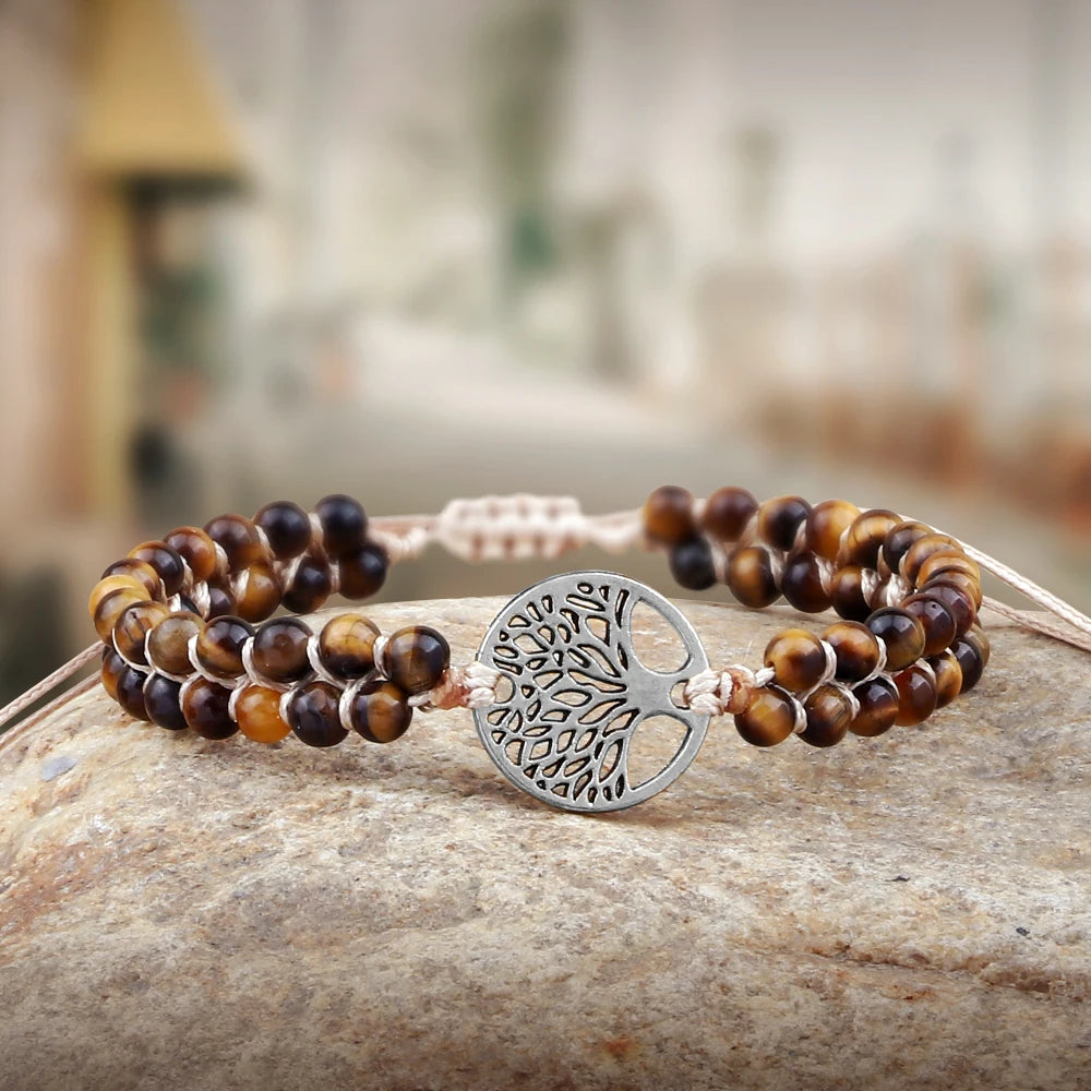 Two beaded bracelets with a silver tree of life charm on a stone surface.