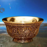 Decorative bronze bowl with intricate patterns on a reflective surface.