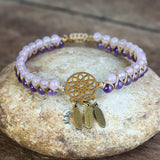 Bracelet with purple beads and gold dreamcatcher charm on a stone surface