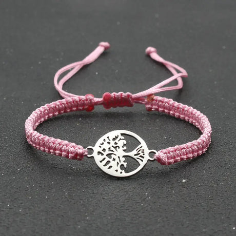 Pink braided bracelet with a silver tree of life charm on a dark background