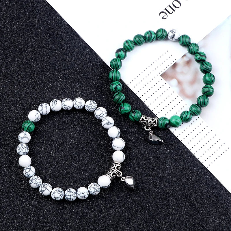 Two beaded bracelets, one green and silver, the other white and silver, on a black and white patterned surface.