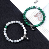 Two beaded bracelets, one green and silver, the other white and silver, on a black and white patterned surface.