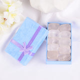 Set of white stones in a blue gift box with a purple ribbon on a white background with flowers.