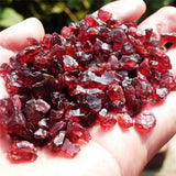 Hand holding red crystals with a blurred natural background