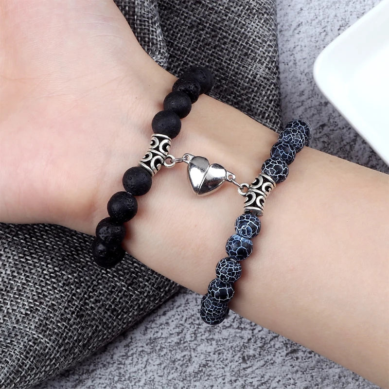 Bracelet with black beads and silver heart charm on a wrist against a gray fabric background