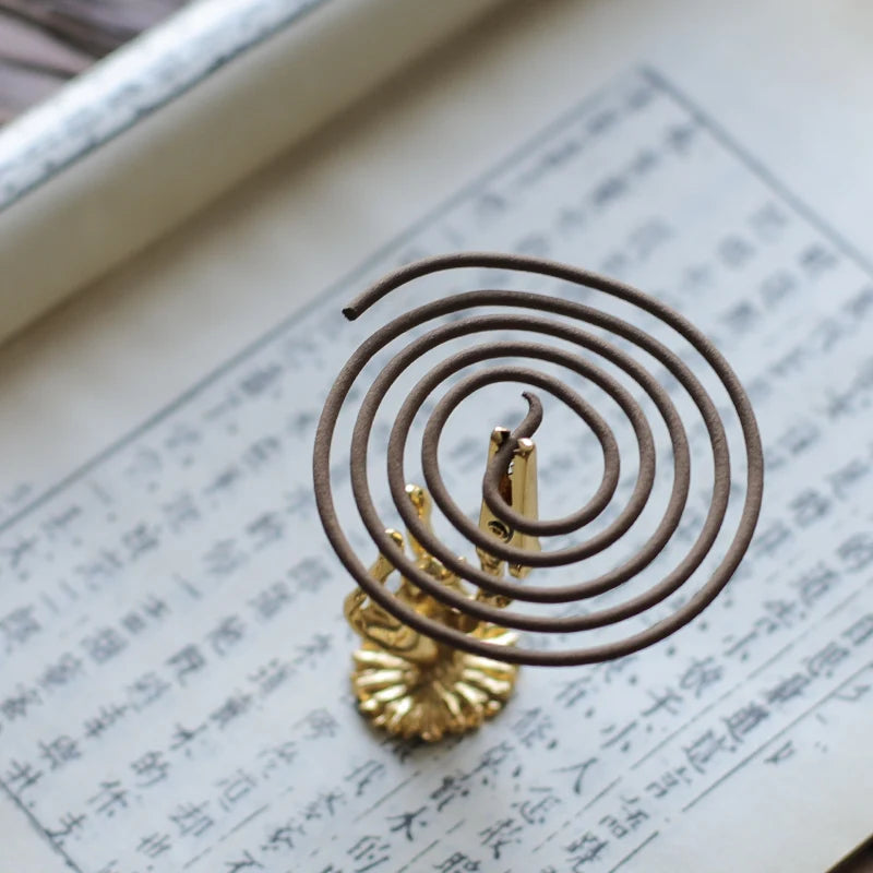 Coiled incense stick on a gold holder over an open book with text.