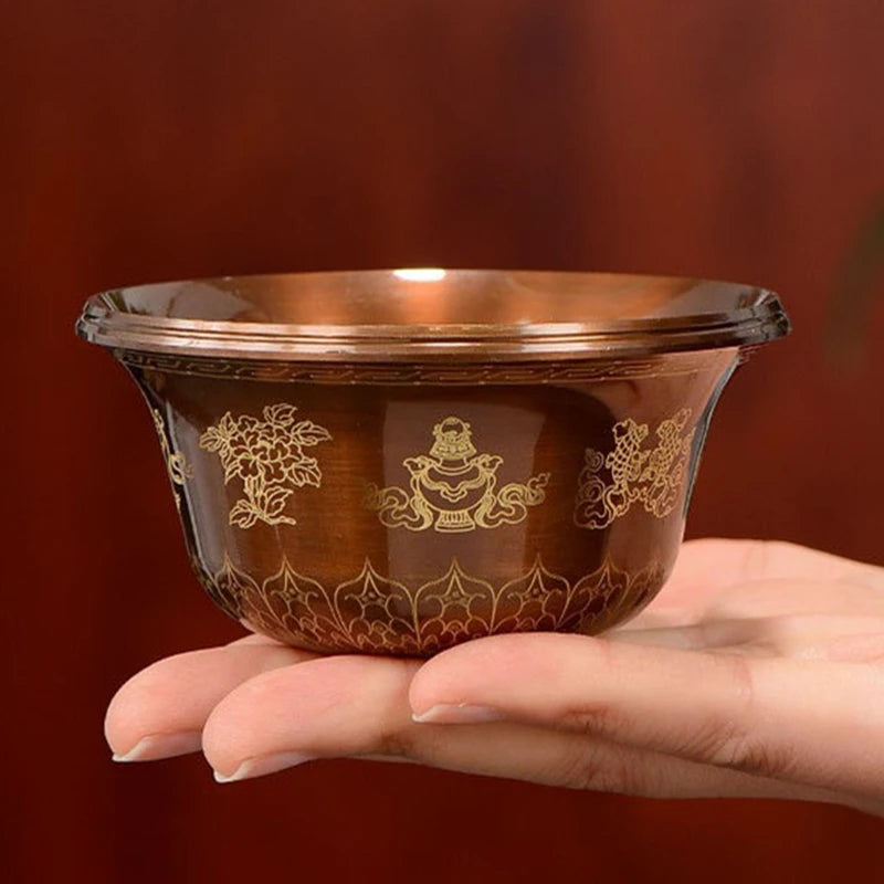 Hand holding a decorative glass bowl with gold patterns against a brown background