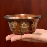 Hand holding a decorative glass bowl with gold patterns against a brown background