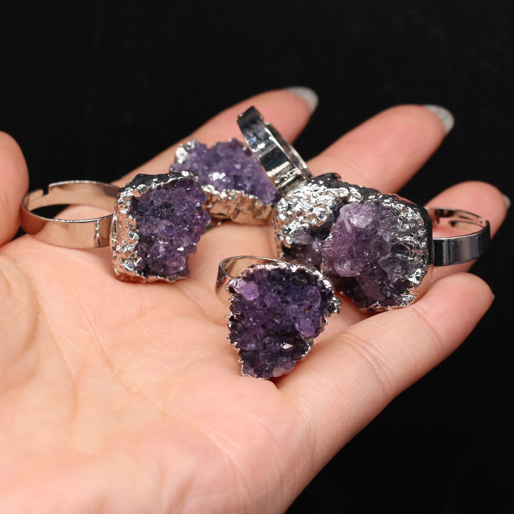 Hand holding purple crystal jewelry pieces against a black background