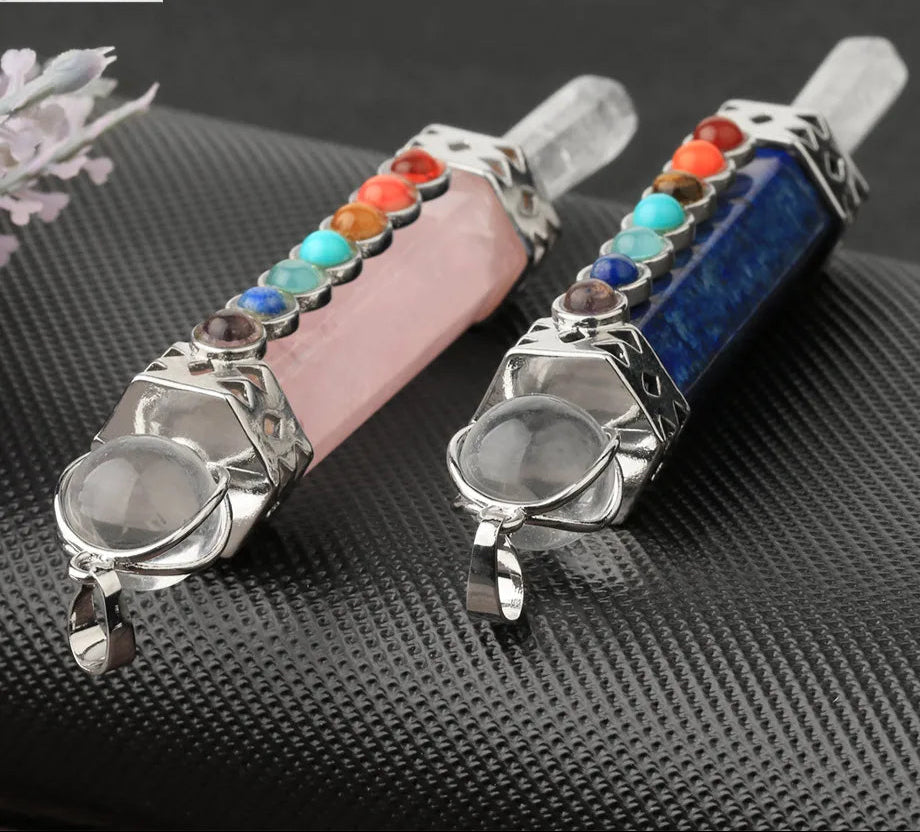 Two crystalpendants with embedded stones on a textured black surface, featuring the Cシア Jewelry logo.