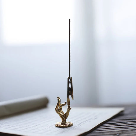 Bronze incense holder with a tall black incense stick on a white surface.