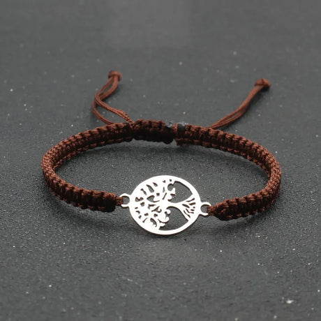Brown braided bracelet with a silver tree of life charm on a dark surface