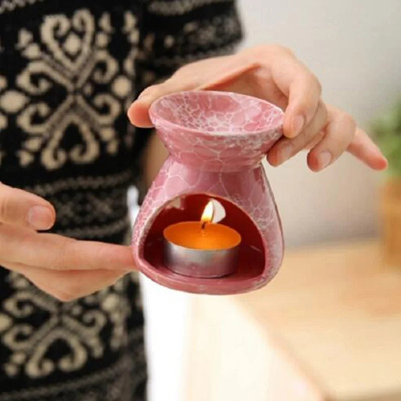 Pink ceramic oil burner with a lit candle inside, held by hands against a blurred background.