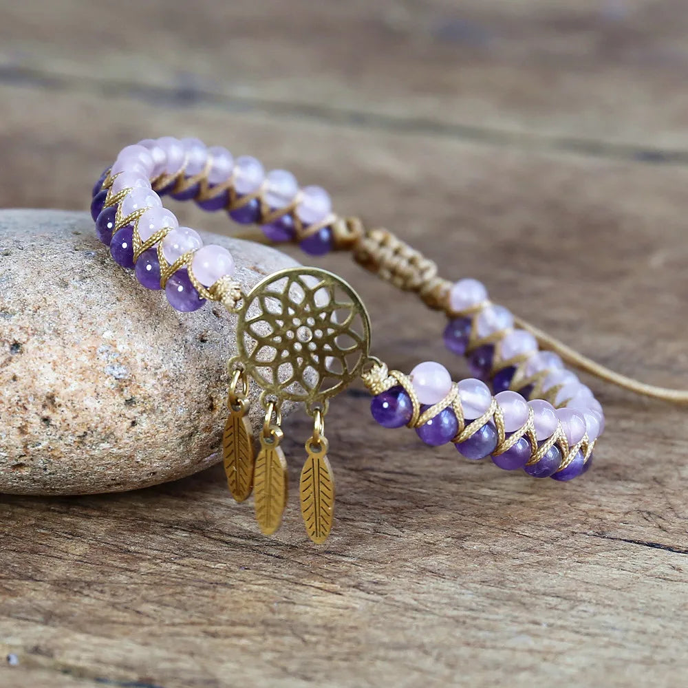 Bracelet with purple and white beads and gold dreamcatcher charm on a wooden surface