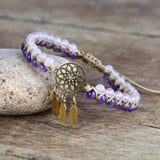 Bracelet with purple and white beads and gold dreamcatcher charm on a wooden surface