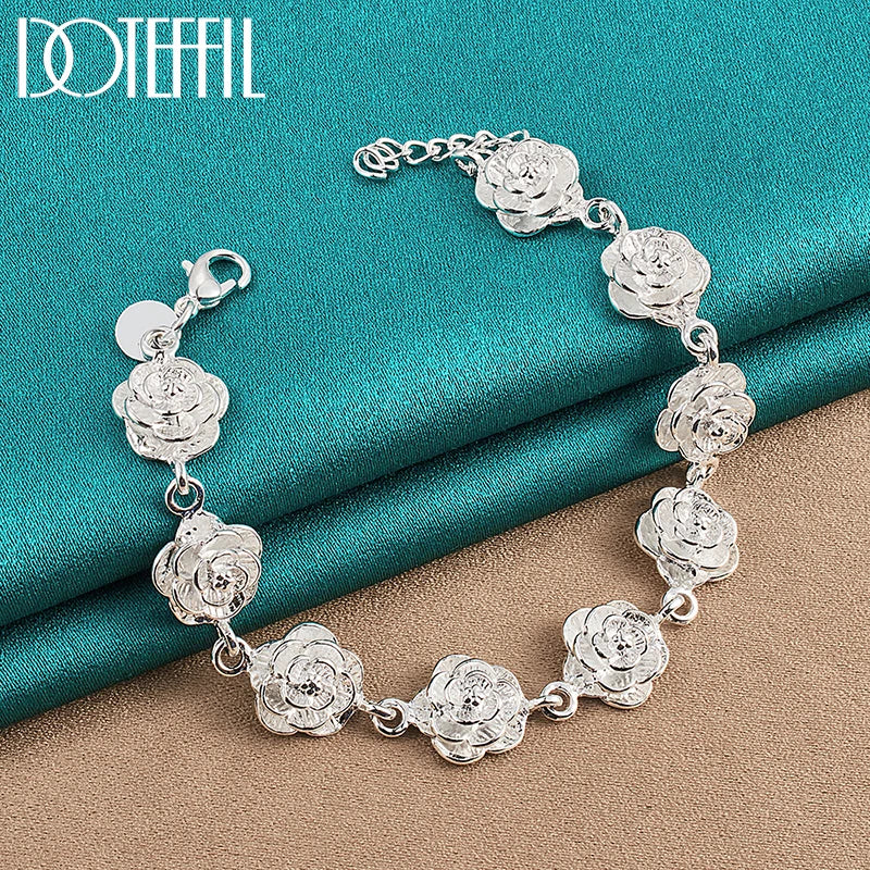 Silver rose bracelet on a teal and beige fabric background with 'DOVEFIL' branding.